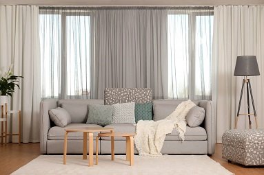 Sheer gray curtains behind light sofa in bright living room
