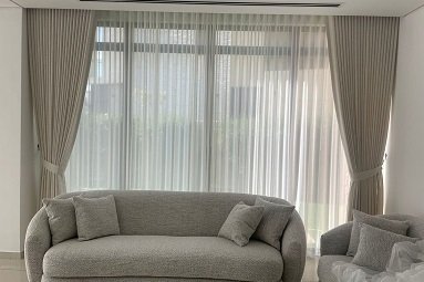 Taupe curtains with sheer layer behind gray sofa in living room
