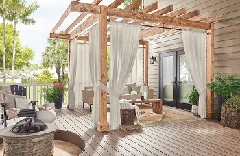 White sheer outdoor curtains hanging from wooden pergola over patio seating area